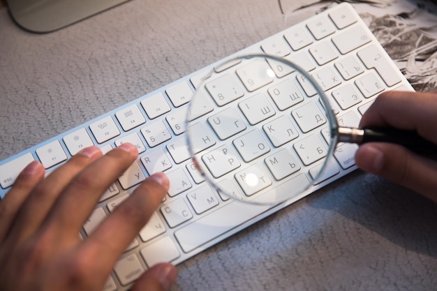A close-up shot of hands typing on a laptop keyboard, with a magnifying glass hovering over the screen, symbolizing the search for unclaimed funds. The focus is on the hands and keyboard, creating a sense of investigation and discovery.