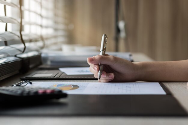 A close-up shot of a hand holding a pen over a printed tax form, with various financial documents and a calculator in the blurred background.