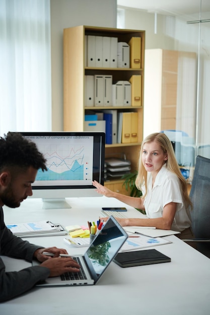 A brightly lit office scene with employees collaboratively working on laptops and reviewing financial reports, highlighting teamwork and analytical thinking.